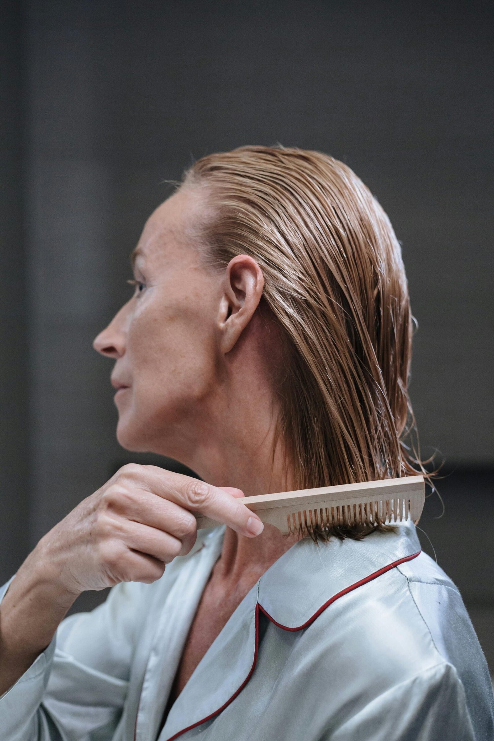 Elderly Caucasian woman combing wet hair in a self-care routine, wearing pajamas.