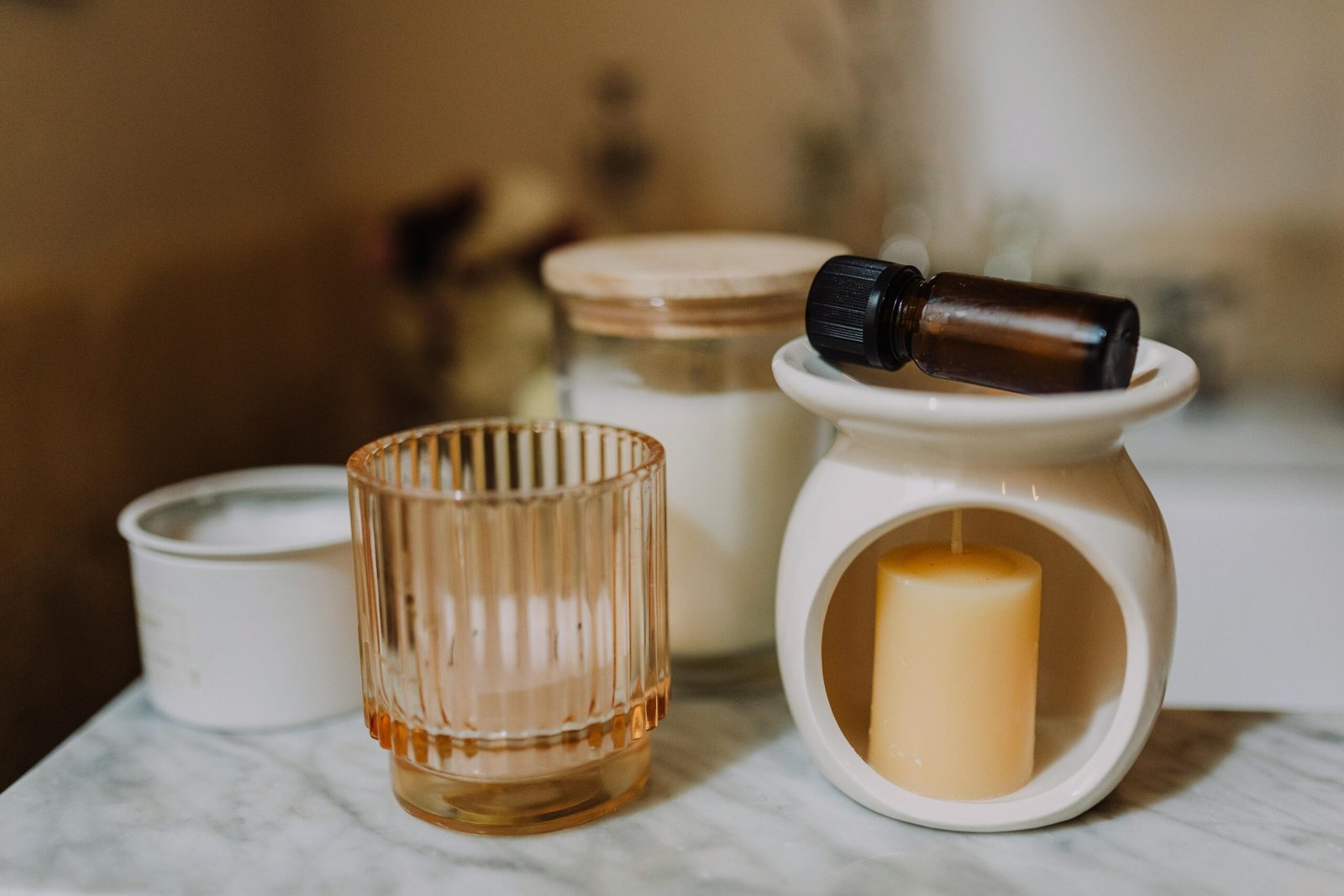 A serene aromatherapy arrangement with candles, glass jars, and essential oil on marble.